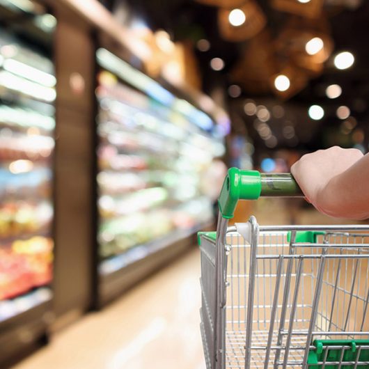 woman hand hold supermarket shopping cart with abstract blur organic fresh fruits and vegetable on shelves in grocery store defocused bokeh light background